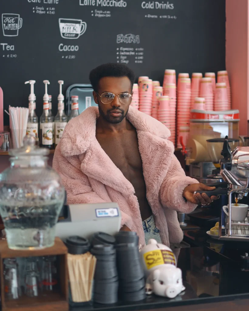 artistic portrait photography of a man in a pink furry coat making coffee in a barista cafe