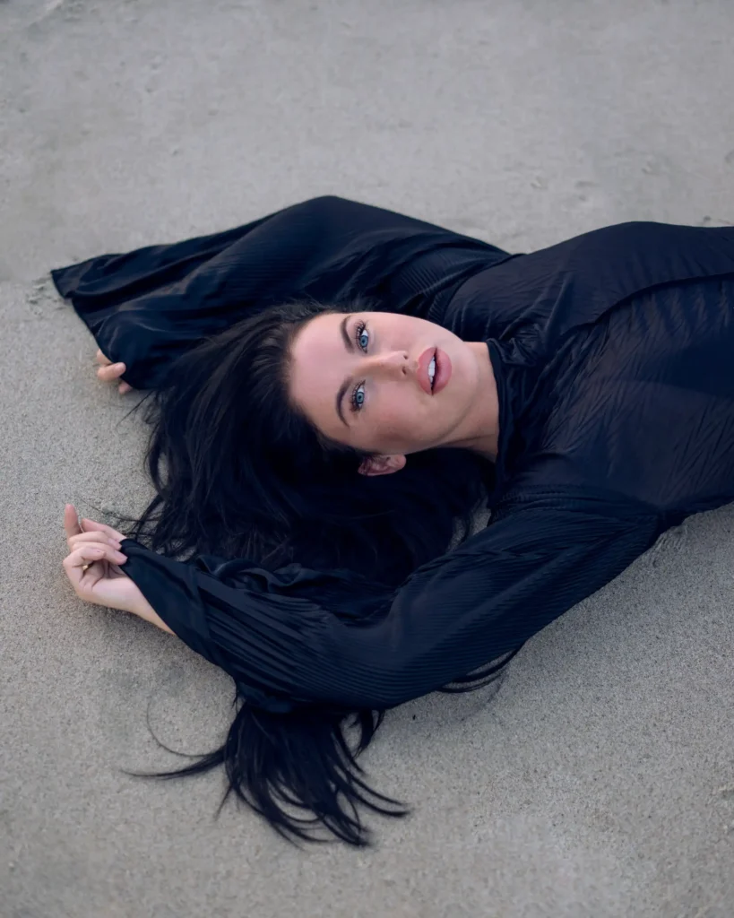 artistic portrait photography of a woman lying on the beach dressed in a black dress