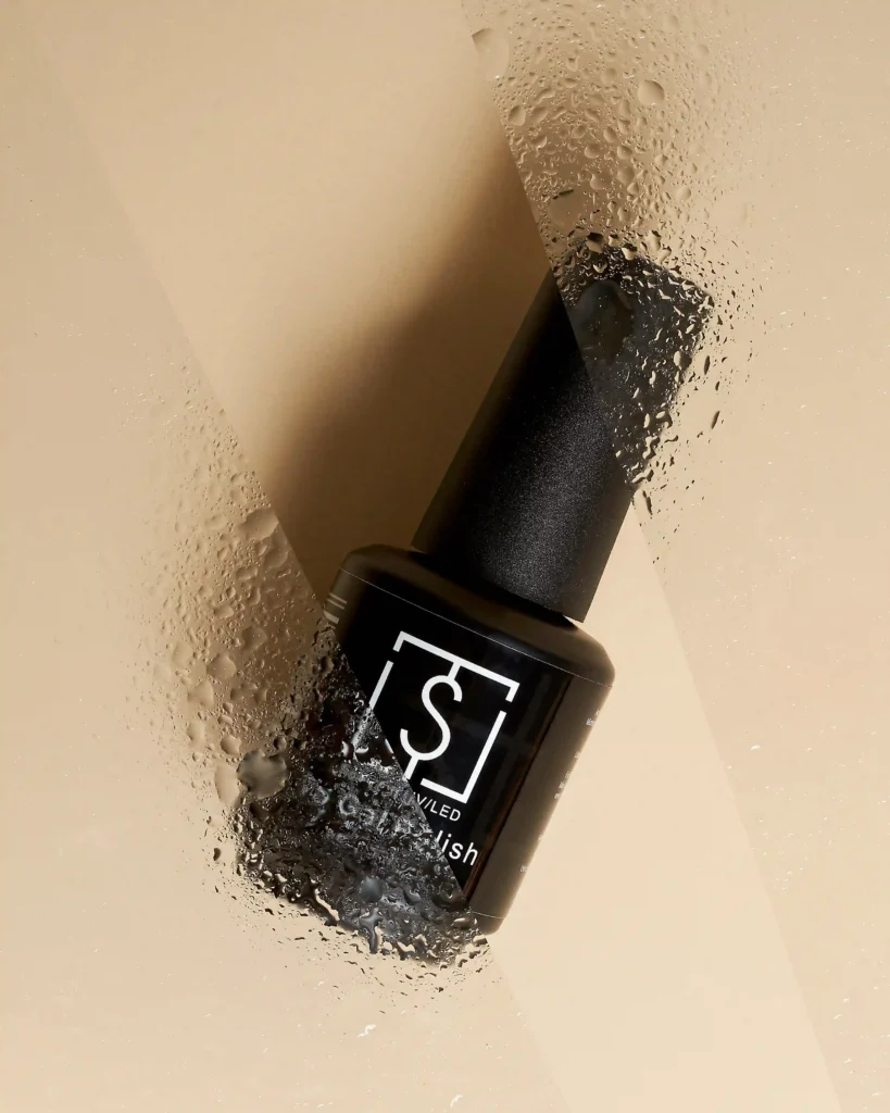 creative still life close up photography of nail polish bottle on the beige background with water drops